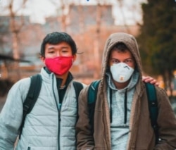 Two young men cover their faces with masks during the coronavirus pandemic. (Photo courtesy of Nico Zviovich)