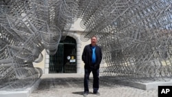 Seniman pembangkang China, Ai Weiwei berpose dengan karyanya "Forever Bicycles" dalam kunjungan khusus pers untuk pameran barunya "Rapture" di Lisbon, Kamis, 3 Juni 2021. (AP Photo/Armando Franca)
