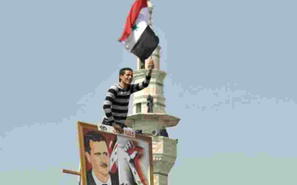 A Syrian man waves the national flag while holding a picture of Syria's President Bashar al-Assad during a pro-government rally at the central bank square in Damascus March 29, 2011. Assad accepted his government's resignation on Tuesday after nearly two