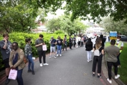 FILE - People queue outside a vaccination center for those aged over 18 years old at the Belmont Health Centre in Harrow, in London, Britain, June 6, 2021.