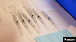 ARCHIVO - Un puñado de jeringuillas listas para ser administrdas vistas en un centro de vacunación de Michigan, EEUU, en abril de 2022.