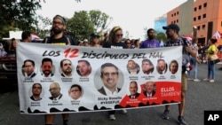  Protesters demanding the resignation of Justice Secretary Wanda Vazquez hold a banner featuring resigned Gov. Ricardo Rossello(C)and other politicians that reads in Spanish 'The 12 disciples of evil. Them too', San Juan, Puerto Rico, July 29, 2019.