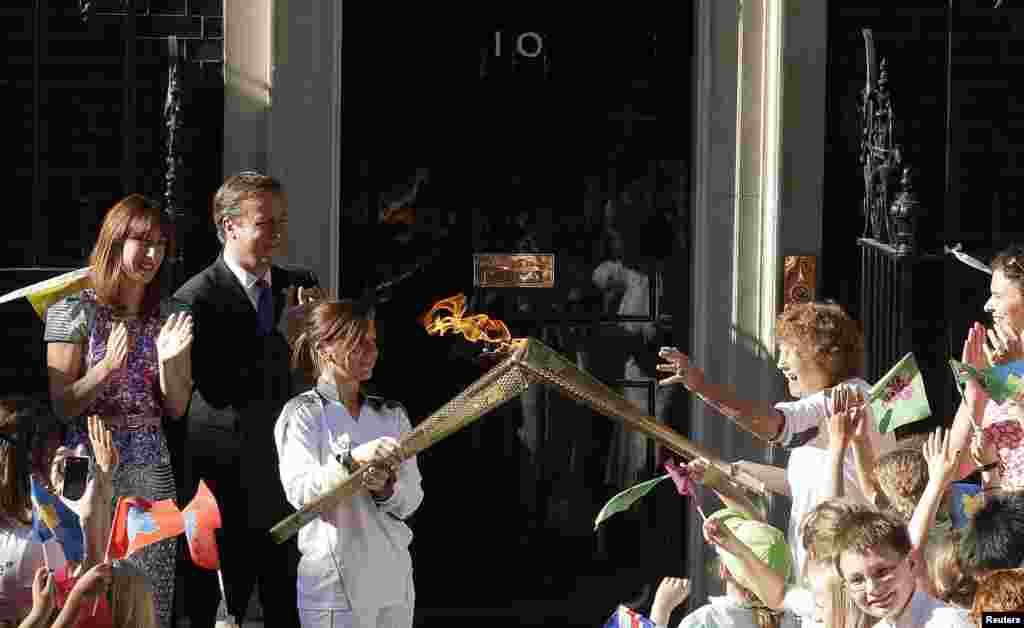 Perdana Menteri Inggris David Cameron (kedua dari kiri) dan istrinya Samantha (kiri) bersama pembawa obor Olimpiade Florence Rowe (kanan) yang mendapat operan api dari Kate Nesbitt di Downing Street (26/7). 