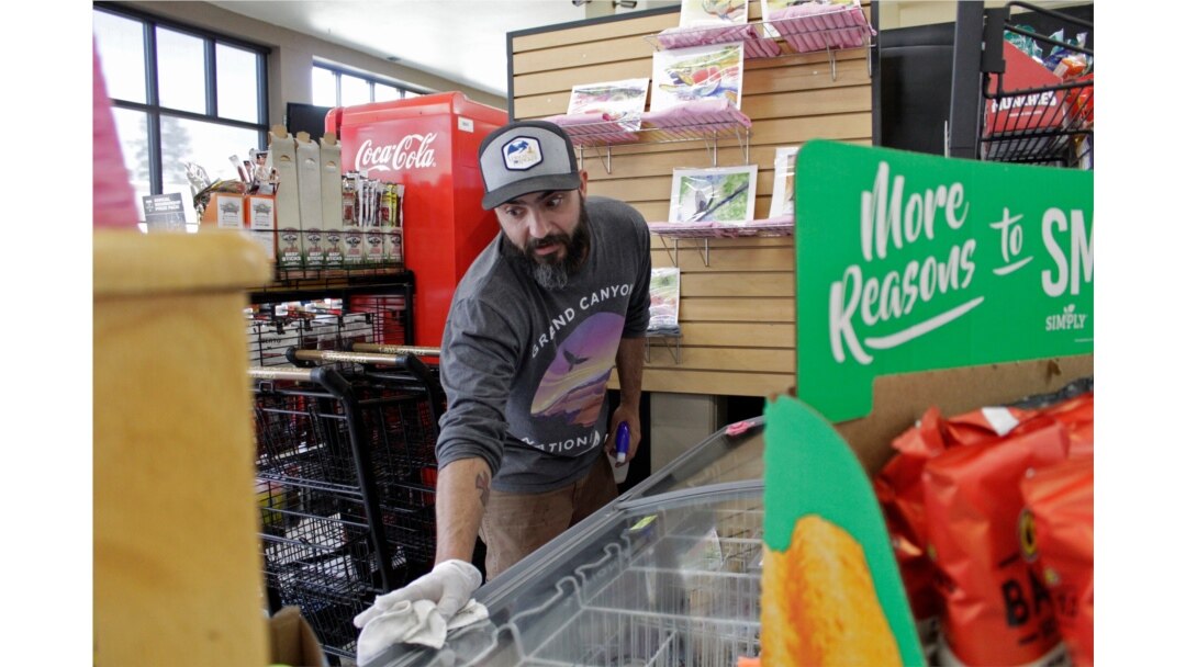 In this photo taken March 20, 2020, Mike Johnston, a clerk at the Maupin Market in Maupin, Oregon, wipes down the ice cream case to protect customers from the coronavirus.