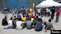 FILE - Migrants sit after disembarking from a merchant ship at the Sicilian harbor of Catania, southern Italy, May 5, 2015. 