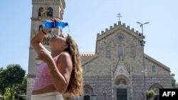 A girl pours a bottle of water on her face and head as she cools off in front of a church in the centre of Messina, on the island of Sicily, during a heat wave on July 16, 2023.