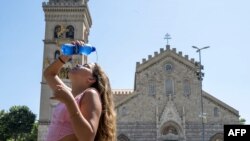 意大利西西里岛一座教堂前，一个姑娘往头上浇水祛暑。（2023年7月16日）