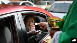 Pastor Jonathan Gonzalez memberikan sakramen Ekaristi kepada seorang jemaah saat Misa Minggu lantatur di halamana parkir gereja, untuk mencegah penularan virus corona di kawasan El Paraiso, Caracas, Venezuela, 25 Oktober 2020. (Foto: AP)