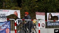 A cyclist rides past damaged electoral posters in Warsaw, Poland, Oct. 14, 2019. 