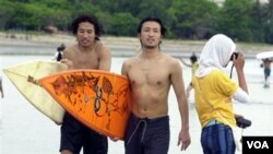 Dua turis Jepang berjalan di pinggiran pantai Kuta, Bali, usai berselancar (foto: dok).