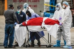 A body wrapped in plastic is unloaded from a refrigerated truck by medical workers wearing personal protective equipment due to COVID-19 concerns, March 31, 2020, at a hospital in New York.