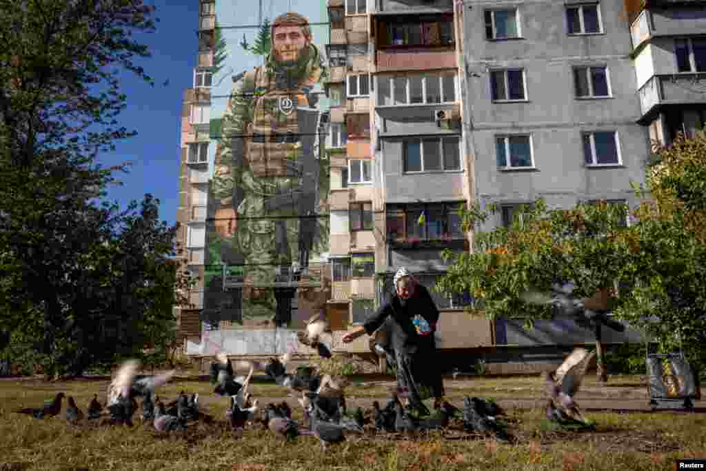 Una mujer alimenta a las palomas frente a un mural del artista ucraniano Eugene Gladenko, en Kiev, Ucrania, el 8 de octubre de 2024.