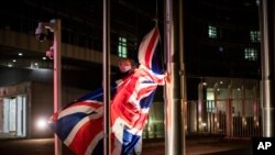 FILE - A worker raises a British flag prior a meeting between European Commission President Ursula von der Leyen and British Prime Minister Boris Johnson at EU headquarters in Brussels, Belgium, Dec. 9, 2020. 