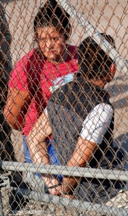 FILE - A handcuffed woman stares though the chain link fencing at Koch Foods Inc. in Morton, Miss., Aug. 7, 2019.