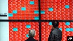 People wearing protective masks watch an electronic stock board showing Japan's Nikkei 225 index at a securities firm, Feb. 8, 2021, in Tokyo. 