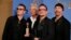 FILE - Adam Clayton (L), Bono (2nd from R), Larry Mullen, Jr. and The Edge (R) from the band U2 pose backstage with their award for Best Original Song, Jan. 12, 2014.
