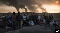 Kaum pria ditahan oleh agen keamanan nasional Irak, guna diinterogasi di titik pemeriksaan, sementara ladang minyak terbakar (5/11) di Qayara, Selatan Mosul, Irak. (foto: AP Photo/Felipe Dana)