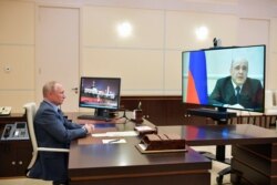 Russian President Vladimir Putin listens to Russian Prime Minister Mikhail Mishustin, displayed on TV screen on the right, during their meeting via teleconference at the Novo-Ogaryovo residence outside Moscow, Russia, April 30, 2020.