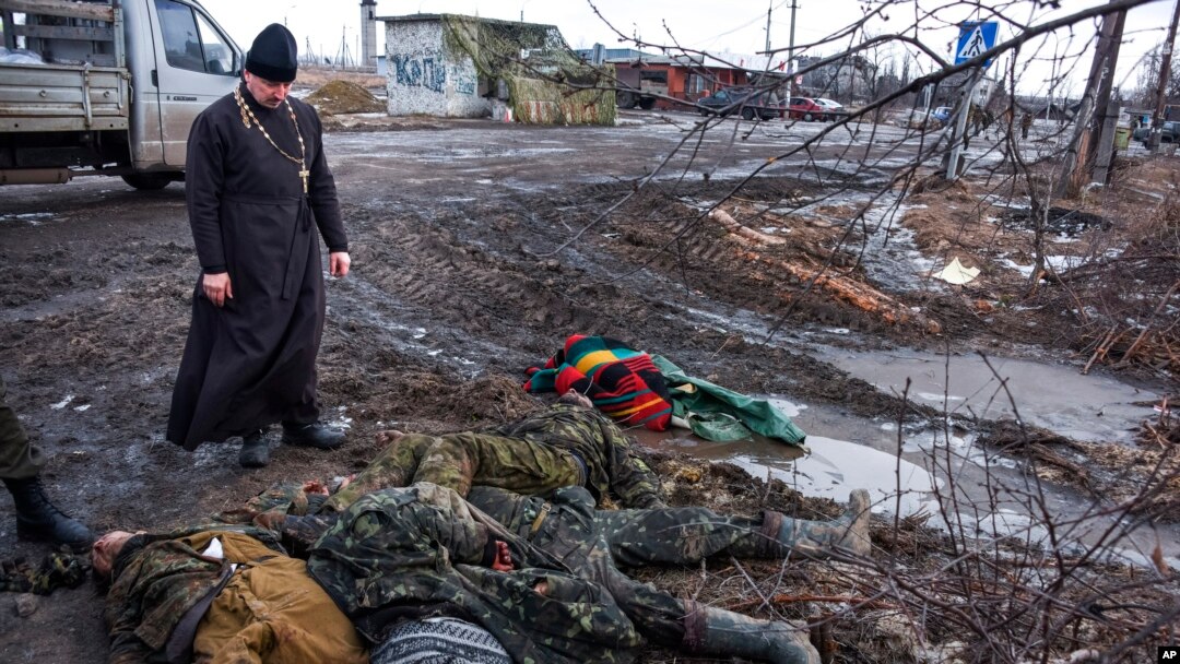 FILE - An Orthodox priest views bodies of killed Ukrainian soldiers at a checkpoint captured by pro-Russian rebels at the eastern Ukraine town of Krasniy Partizan, Jan. 24, 2015. Fighting has eased but continues despite several cease-fires.
