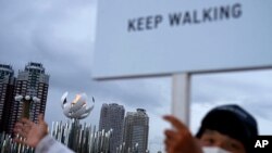 A worker urges pedestrians to keep walking outside an Olympic flame as part of a COVID-19 precautions during the 2020 Summer Olympics, Aug. 2, 2021, in Tokyo.