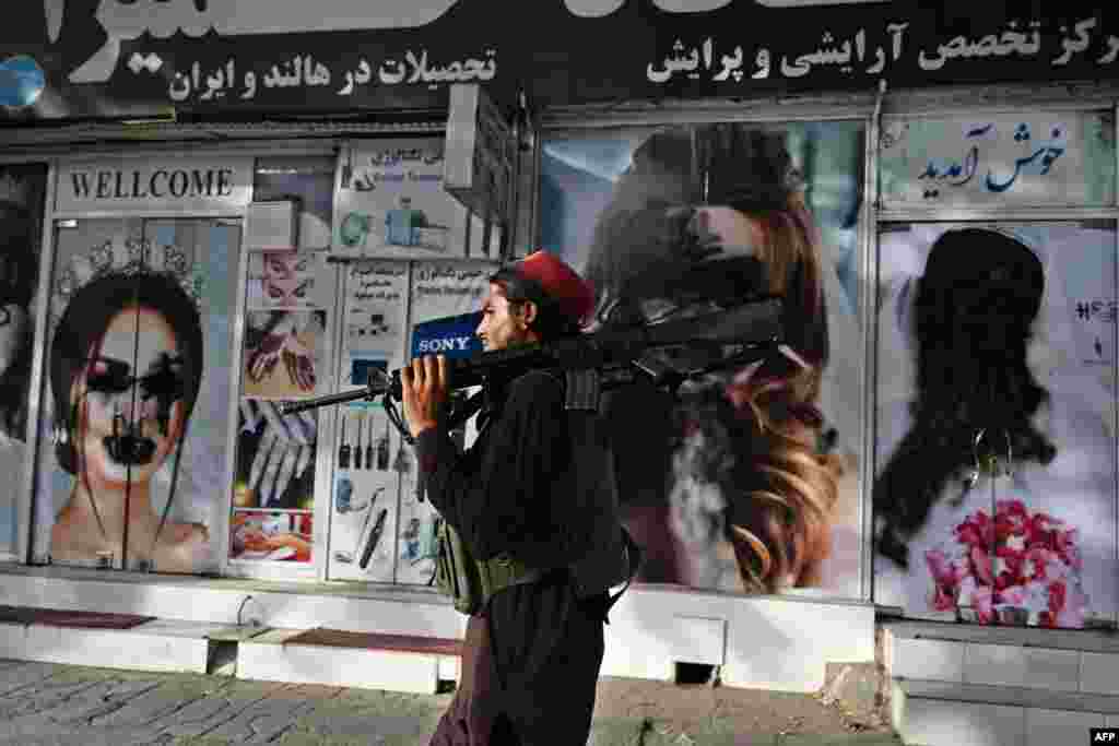 A Taliban fighter walks past a beauty salon with defaced posters in Shar-e-Naw in Kabul, Afghansitan, Aug. 18, 2021.