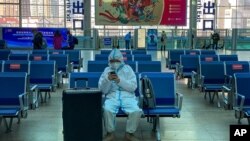 Un viajero con equipo de protección para ayudar a frenar la propagación del coronavirus se sienta solo en un banco mientras espera el tren en una estación del sur de Beijing, el jueves 28 de enero de 2021.