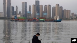 FILE - A man wearing a mask against the new coronavirus checks his phone as a container ship cruises along the Yangtze River in Wuhan in Central China's Hubei province, April 13, 2020.