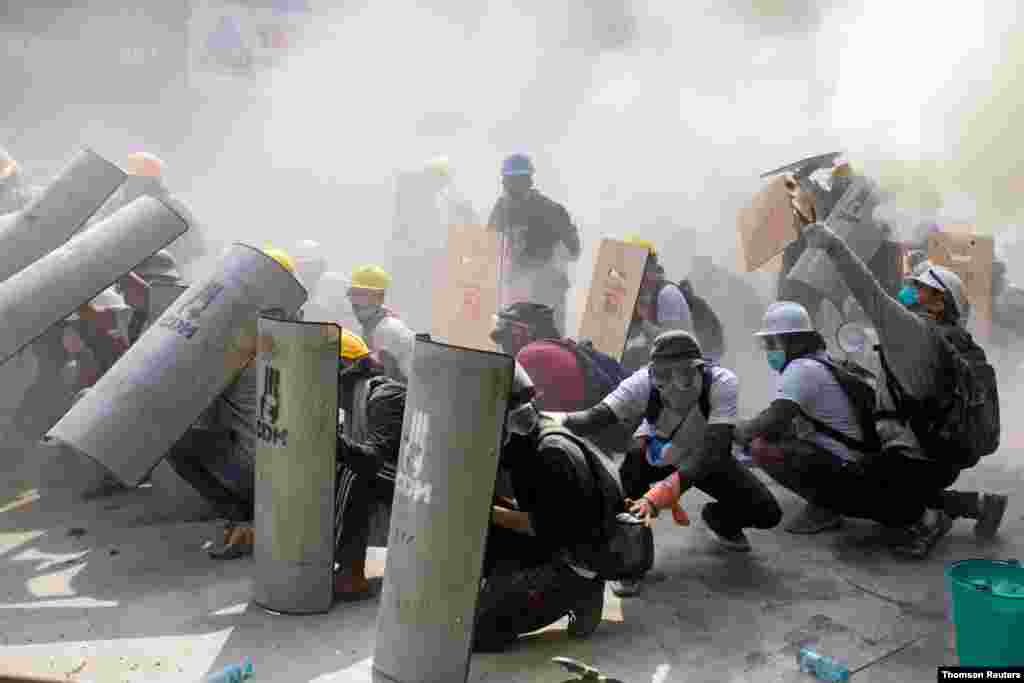 Protesters take cover as they clash with riot police officers during a protest against the military coup in Yangon, Myanmar, Feb. 28, 2021. 