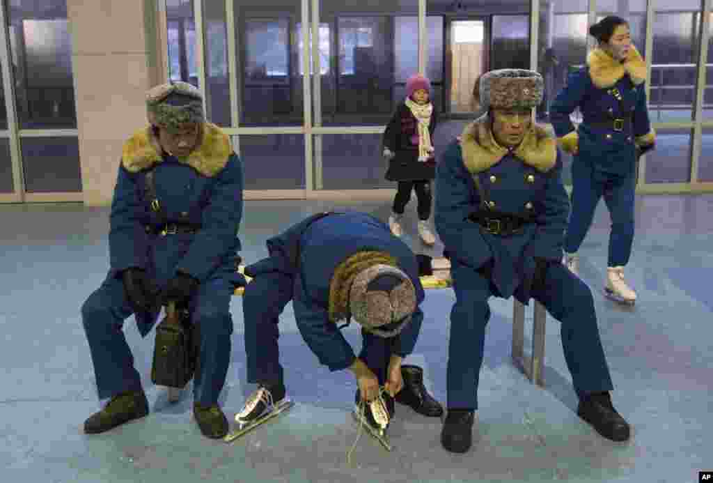 An off-duty North Korean traffic policeman laces up ice skates as his colleagues sit near by at an ice skating rink in Pyongyang. 