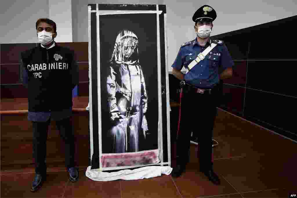 Italian Carabinieri pose near a piece of art attributed to Banksy, that was stolen at the Bataclan in Paris in 2019, and found in Italy, during a press conference in L&#39;Aquila.