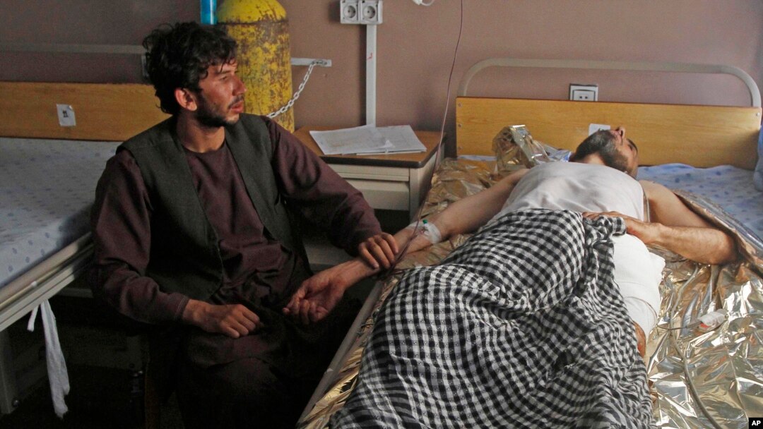 An Afghan wounded man, right, lies on the bed in a hospital as his relative sits on a chair beside him in the city of Kandahar, south of Kabul, Afghanistan, July 9, 2014. 