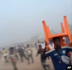 En esta imagen tomada de un video proporcionado por Nimba Sports Zaly, un hombre sostiene una silla sobre su cabeza durante una estampida en un partido de fútbol en el estadio de Nzérékoré, en Nzérékoré, Guinea, el 1 de diciembre de 2024. (Nimba Sports Zaly via AP)