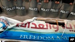 FILE - Egyptian anti-riot soldiers stand guard in front of a destroyed banner of the Muslim Brotherhood's Freedom and Justice Party, March 2013.