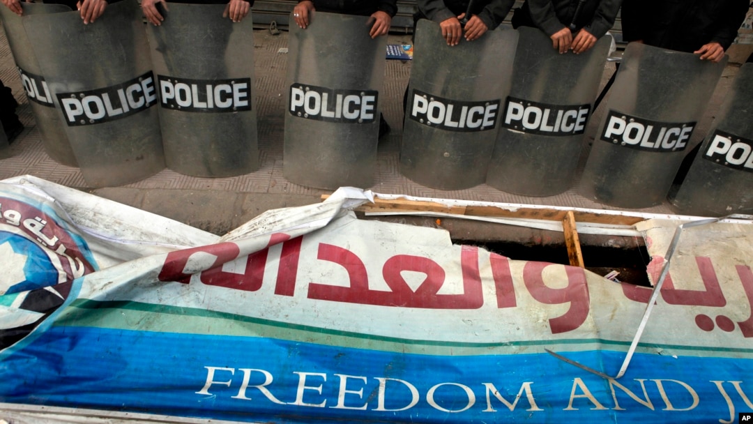 FILE - Egyptian anti-riot soldiers stand guard in front of a destroyed banner of the Muslim Brotherhood's Freedom and Justice Party, March 2013.