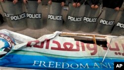 FILE - Egyptian anti-riot soldiers stand guard in front of a destroyed banner of the Muslim Brotherhood's Freedom and Justice Party, March 2013.