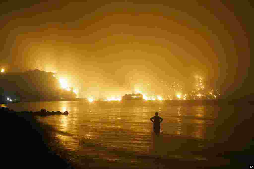 A man watches as a wildfire approaches Kochyli beach near the village of Limni, Greece, about 160 kilometers (100 miles) north of Athens, Greece, Aug. 6, 2021.