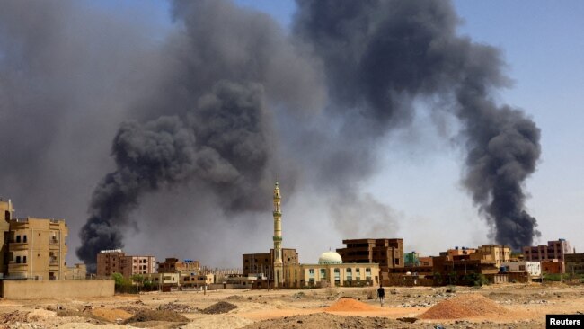 FILE - A man walks while smoke rises above buildings after aerial bombardment, during clashes between the paramilitary Rapid Support Forces and the army in Khartoum North, Sudan, May 1, 2023.