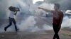 A protester argues with law enforcement officers as a reporter runs from tear gas during a demonstration in Saint Paul, Minnesota, May 31, 2020, against the death in Minneapolis police custody of George Floyd. 