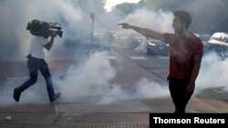 A protester argues with law enforcement officers as a reporter runs from tear gas during a demonstration in Saint Paul, Minnesota, May 31, 2020, against the death in Minneapolis police custody of George Floyd. 