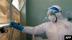 FILE - A medical staff member wears protective equipment while closing a window at the Wilkins Infectious Diseases Hospital in Harare, March 11, 2020.