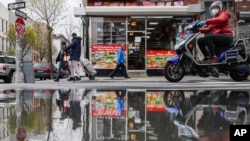 Pedestrians and motorists wear personal protective equipment as they pass a small grocery that is one of the few businesses open on the street, April 27, 2020, in the Brooklyn borough of New York.
