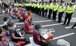 Extinction Rebellion climate activists sit in the road and meditate in front of a line of police officers outside of Parliament during a "peaceful disruption" of British Parliament in London, Sept. 1, 2020.