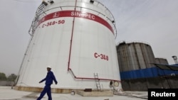 FILE - An employee walks past oil tanks at a Sinopec refinery in Wuhan, Hubei province April 25, 2012. China’s top state-owned refiners have decided not to order any oil for loading at Iranian ports this month, according to Reuters.