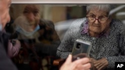 Javier Anto (90), menunjukkan foto cucunya kepada istrinya Carmen Panzano (92), melalui jendela panti wreda di Barcelona, ​​​​Spanyol, di tengah pandemi COVID-19, 21 April 2021. (AP Photo/Emilio Morenatti)