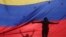 FILE - The silhouettes of anti-government protesters are seen through a Venezuelan flag in Caracas, Venezuela, July 10, 2017. 