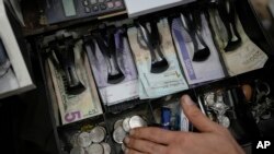 Un vendedor muestra los bolívares y los dólares en su caja registradora en un mercado público en Caracas, el martes 18 de enero de 2022. 