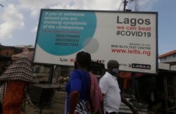 FILE - Pedestrians walk past a sign telling residents to call phone numbers if they have symptoms of COVID-19, the disease caused by the coronavirus, in Lagos, Nigeria, May 12, 2020.