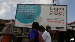 FILE - People walk past a sign advising residents to report if they have coronavirus symptoms, in Lagos, Nigeria, May 12, 2020.