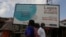 FILE - People walk past a sign advising residents to report if they have coronavirus symptoms, in Lagos, Nigeria, May 12, 2020.