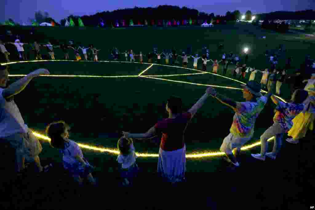 People hold hands in a circle around a large, lit peace sign on the site of the 1969 Woodstock Music and Arts Fair in Bethel, New York, Aug. 15, 2019.